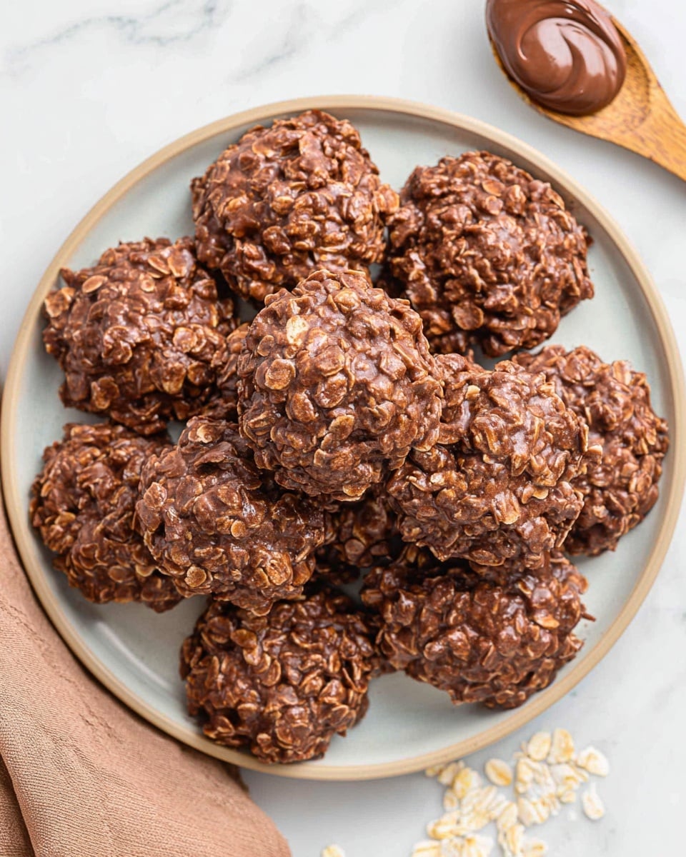 The image shows a plate filled with delicious no-bake chocolate oatmeal cookies, featuring a rich, fudgy texture with visible oats mixed throughout. The cookies appear moist and chunky, suggesting a creamy chocolate mixture binding the oats together. A wooden spoon with a dollop of chocolate spread rests nearby, hinting at one of the key ingredients used in making these treats. The light background and arrangement of the cookies create an inviting presentation perfect for a sweet snack. photo taken with an iPhone --ar 4:5 --v 7