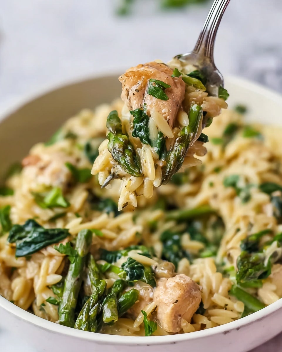 A close-up of a white bowl filled with a creamy dish made of three main layers: the base layer is light golden orzo pasta that looks soft and coated in sauce, the middle layer has chunks of light brown cooked chicken, and the top layer shows bright green asparagus spears and wilted dark green spinach leaves scattered around, all mixed with chopped parsley. A silver fork lifts a bite-sized portion showing all three layers clearly, with the pasta, chicken, leafy spinach, and asparagus appearing fresh and tender. The bowl sits on a white marbled surface with a soft, blurred background. photo taken with an iphone --ar 4:5 --v 7