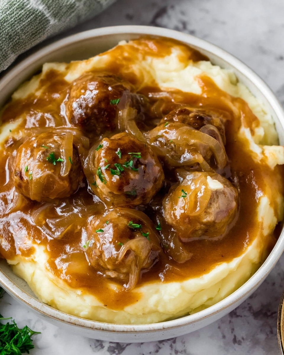 A white bowl filled with three visible layers: the bottom layer is creamy mashed potatoes, smooth and pale yellow in color; above that is a thick brown gravy with visible translucent caramelized onions scattered throughout; the top layer consists of several small round meatballs covered in the same glossy brown gravy with hints of melted cheese on them. A few small green herb pieces garnish the meatballs. The bowl is placed on a white marbled surface with a hint of green herbs in the corner. Photo taken with an iphone --ar 4:5 --v 7