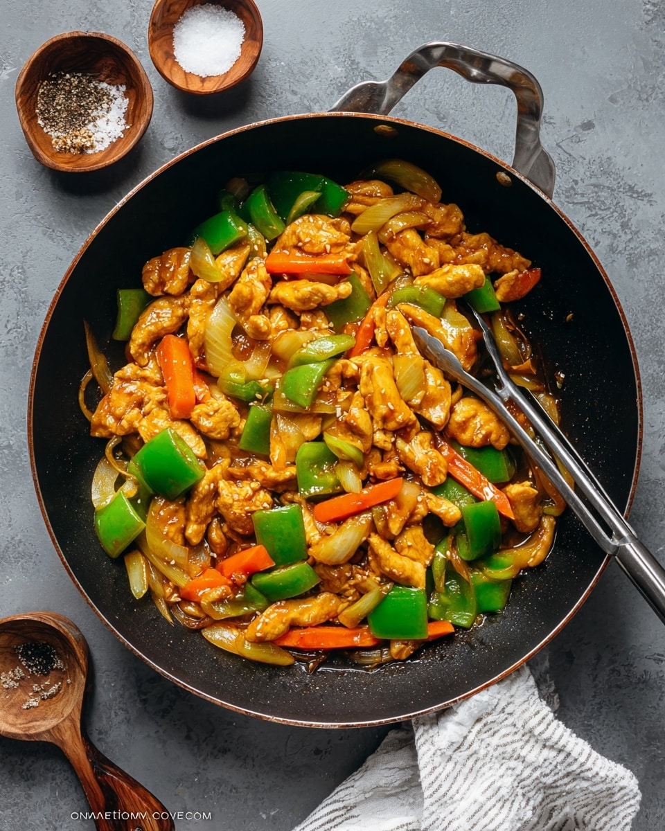 In a large black pan with shiny metal handles, there is a colorful stir-fry. It has three main layers: at the bottom are thick, uneven strips of pale yellow chicken coated in a glossy brown sauce; mixed throughout are chunky pieces of bright green bell pepper with smooth skin; and scattered among them are thin, slanted slices of orange carrot and translucent, diced white onion. The mix looks juicy and hot, with some oil glistening on the vegetables and chicken. A metal cooking tong is resting inside the pan on the right side, partially under the food. The pan sits on a gray textured surface, with two small wooden bowls below, one with coarse salt and a small spoon and the other with black pepper, and a folded white striped cloth is underneath the pan handle on the bottom right. Photo taken with an iphone --ar 4:5 --v 7