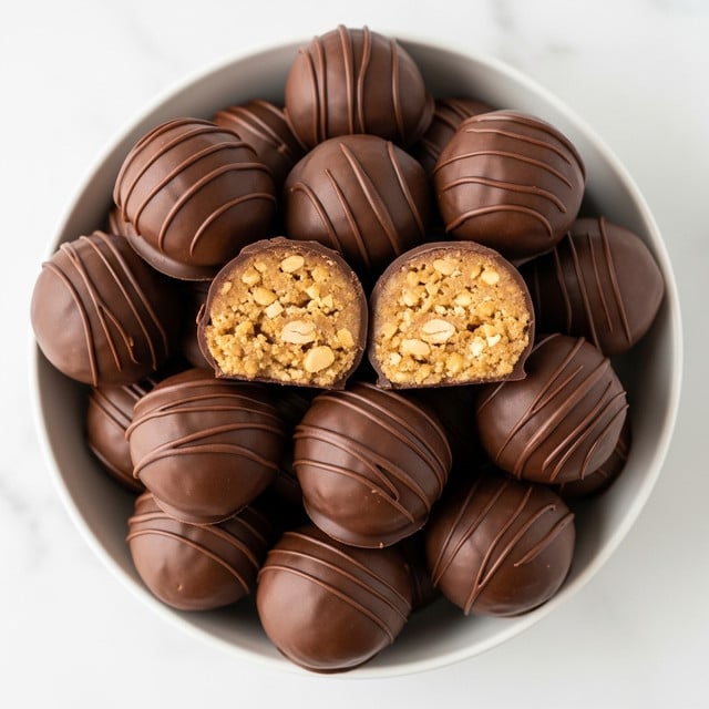 The image shows a white bowl filled with round chocolate-covered peanut butter balls. The outer layer is smooth, dark brown chocolate with a shiny texture. Two of the balls are cut in half and placed on top in the middle, showing the inside with a dense, light golden peanut butter filling mixed with crunchy bits. The arrangement creates a layered look with multiple whole chocolate balls surrounding the halved ones. The bowl sits on a white marbled surface, giving a clean and bright background. photo taken with an iphone --ar 4:5 --v 7