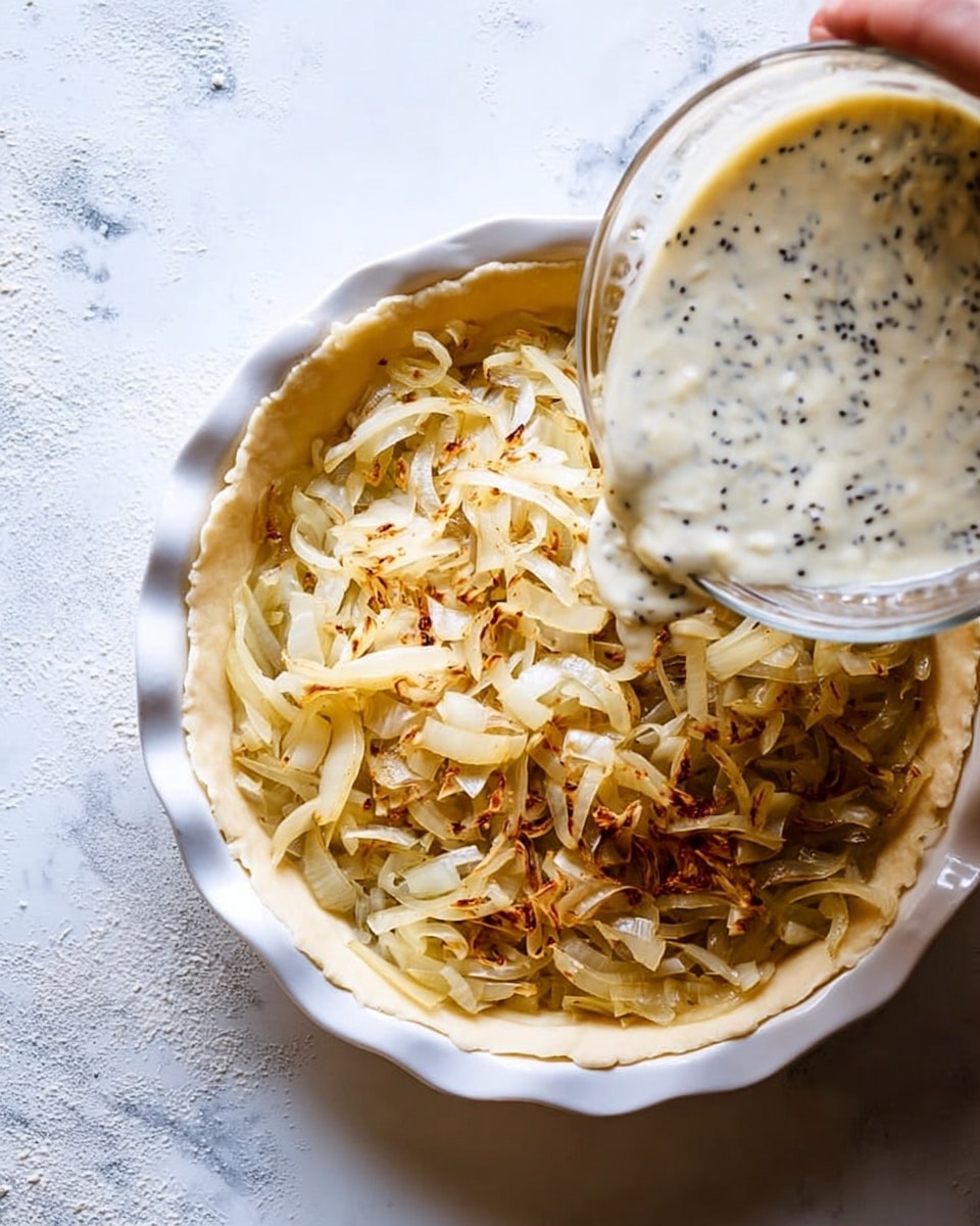 The image shows a close-up of a white round pie dish with a crust base and a layer of cooked, golden-brown sliced onions spread evenly inside. Above, a clear glass bowl held by a woman's hand pours a creamy mixture with visible black seeds onto the onions, about to fill the pie dish. The pie dish sits on a white marbled textured surface with soft natural light highlighting the textures and colors of the onions and creamy mixture. Photo taken with an iphone --ar 4:5 --v 7