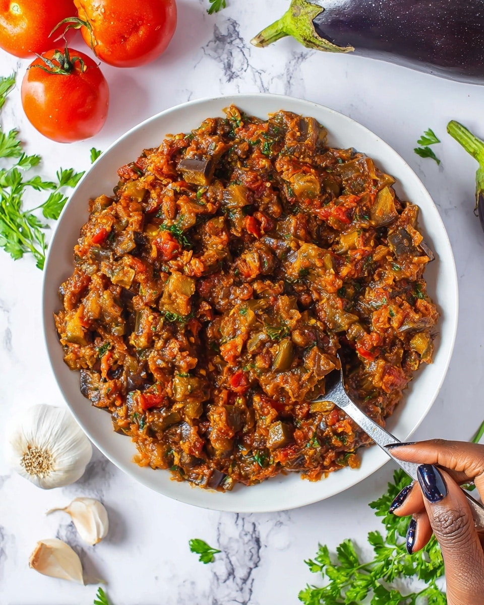 The image shows a close-up of a white plate filled with a chunky, mixed vegetable dish made of small pieces of eggplant, tomato, and herbs combined in a textured, reddish-brown sauce with visible green herb bits scattered throughout. The dish has a layered appearance with uneven chunks creating a rough surface. A woman's hand with dark polished nails holds a spoon, stirring the mixture, adding shine to the dish. Around the plate, there are fresh whole tomatoes, garlic cloves, an eggplant tip, and green parsley leaves, all placed on a white marbled surface. photo taken with an iphone --ar 4:5 --v 7