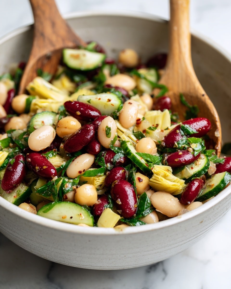 A close-up view of a mixed bean salad in a large white bowl placed on a white marbled surface. The salad has multiple colorful layers including cream-colored cannellini beans, red kidney beans, yellow chickpeas, and chopped light green artichoke hearts. There are also slices of dark green cucumber and pieces of fresh dark green leafy herbs scattered throughout. Two wooden spoons with a smooth texture, one partially submerged and the other resting on the side, are mixing the salad. The overall texture appears fresh and slightly wet, with visible small specks of seasoning or dressing on the ingredients. photo taken with an iphone --ar 4:5 --v 7