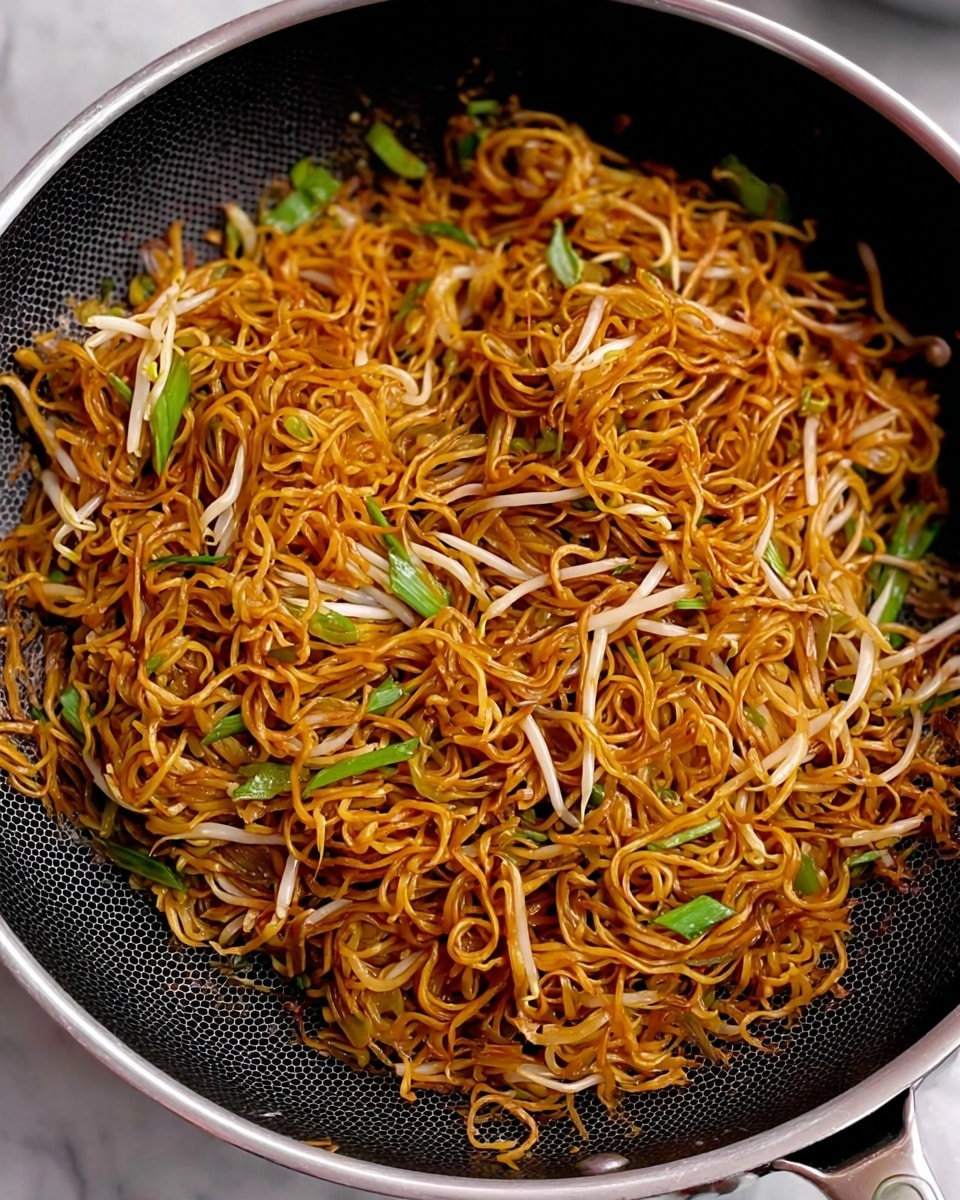 The image shows a pan filled with cooked noodles that are dark golden brown and slightly shiny, mixed with light, translucent bean sprouts and small pieces of green onions. The noodles are thin and tangled together in several layers, creating a textured look. The bean sprouts and green onions are spread throughout, adding contrast to the dense mass of noodles. The pan is black with a subtle hexagon pattern inside and a silver rim, placed on a white marbled surface. photo taken with an iphone --ar 4:5 --v 7