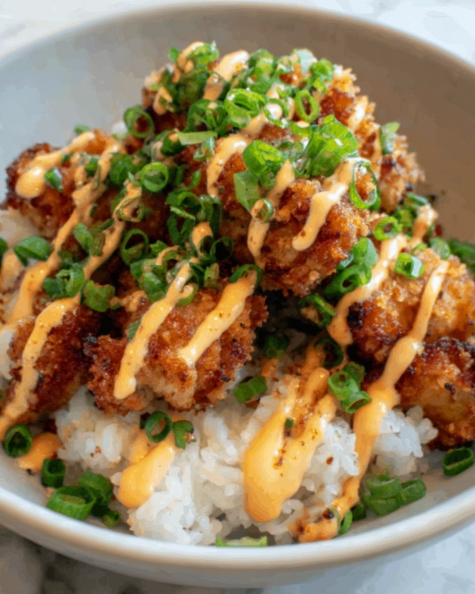 The image shows a white bowl filled with white rice as the bottom layer, topped with crispy fried chicken pieces that have a golden-brown color and a slightly crunchy texture. On top of the chicken, there is a drizzle of light orange creamy sauce, applied in zigzag lines, and a generous sprinkle of chopped fresh green onions, adding a bright green contrast to the dish. The bowl sits on a white marbled surface. Photo taken with an iphone --ar 4:5 --v 7