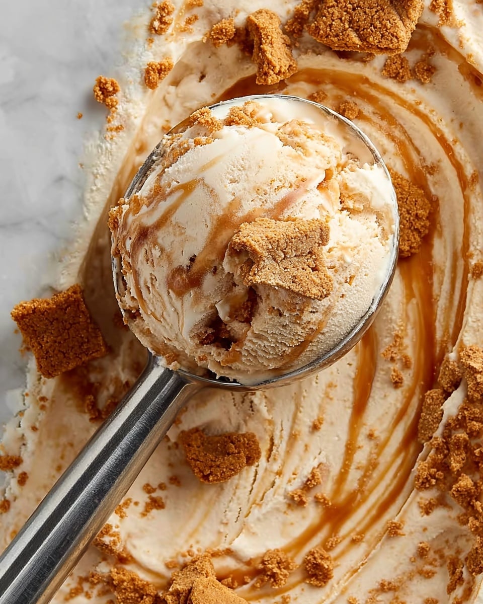 A close-up view of creamy ice cream with visible small chunks, held in a shiny metal ice cream scoop. The ice cream has a smooth beige base with swirls of caramel sauce creating light brown curved lines throughout. Crumbled golden brown cookie pieces are scattered on the ice cream’s surface and mixed into the swirls, adding texture. The background is a white marbled texture serving as the base for the ice cream. Photo taken with an iphone --ar 4:5 --v 7