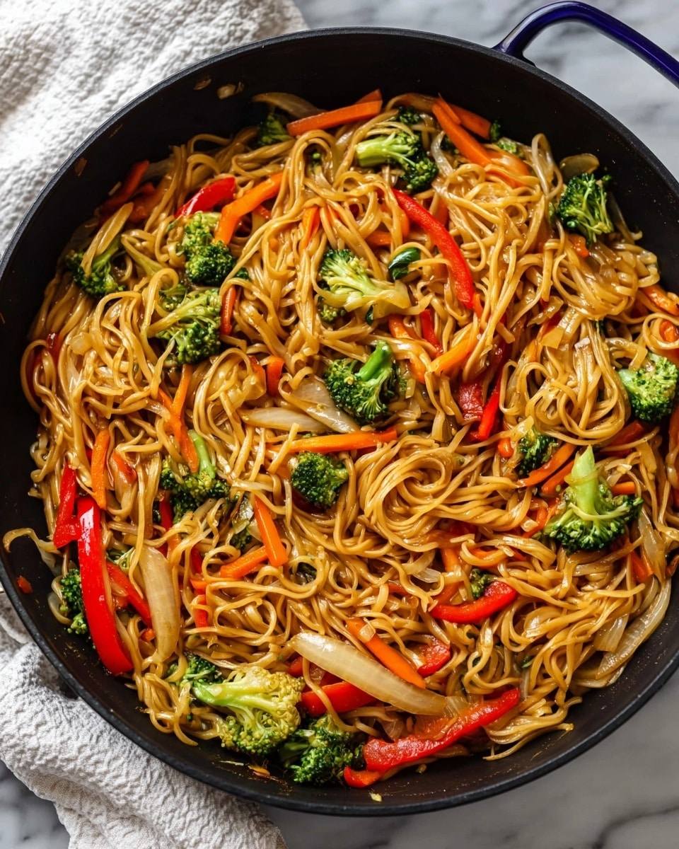 A close-up view of a black pan filled with stir-fried noodles mixed with colorful vegetables. The noodles form the main base layer, light brown and glossy, with long, thin strands tangled together. Scattered throughout are bright green broccoli florets, red bell pepper strips, and thin orange carrot slices, adding vivid color and a crunchy texture. Lightly cooked onion slices add a translucent white touch beneath the noodles. The pan sits on a white marbled surface, and a part of a white cloth can be seen beside it. photo taken with an iphone --ar 4:5 --v 7