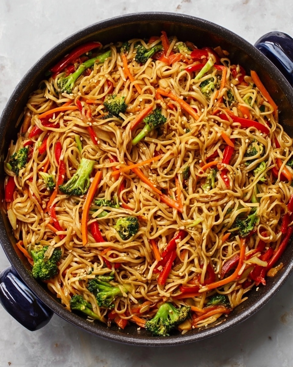 The image shows a round black pan filled with stir-fried noodles. The noodles are light brown and mixed with several colorful layers of vegetables: small bright green broccoli florets, thin red strips of bell pepper, and thin orange carrot sticks, all evenly spread throughout the noodles. The pan is placed on a white marbled surface, which contrasts with the dark color of the pan and makes the food stand out. photo taken with an iphone --ar 4:5 --v 7