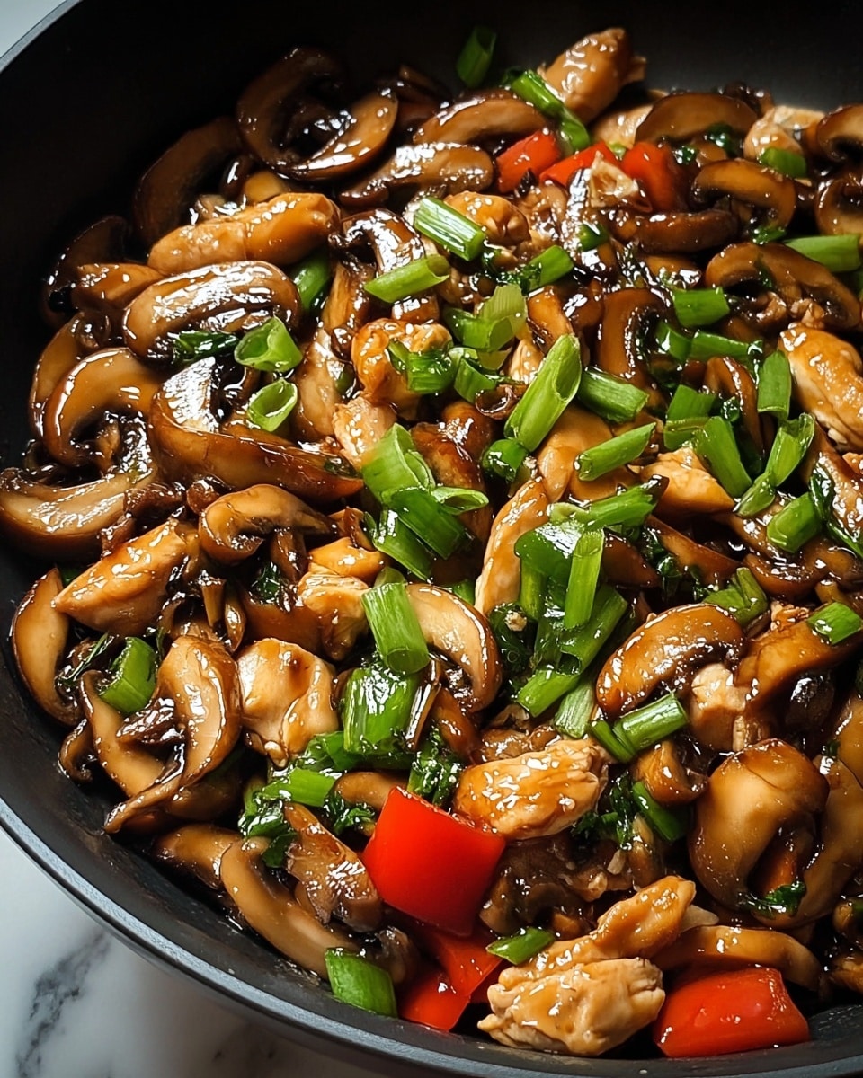 The image shows a close-up of a stir-fry dish in a black pan, filled with glossy, cooked mushroom slices that have a rich brown color and shiny texture. Mixed among the mushrooms are tender pieces of light golden-brown chicken, bright green chopped scallions scattered on top, and small pieces of red bell pepper adding a splash of color. The dish has a moist, slightly oily look, highlighting the sauce coating all the ingredients. The background is a white marbled texture. Photo taken with an iphone --ar 4:5 --v 7