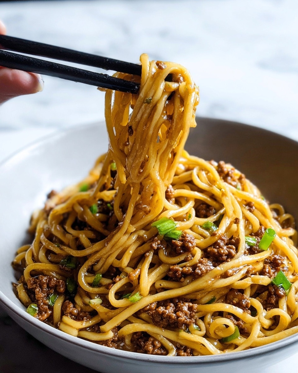 A close-up view of a bowl filled with thick light yellow noodles mixed with dark brown minced meat and small pieces of green onion scattered throughout. The noodles are coated with a glossy sauce, and some noodles are lifted by black chopsticks held by a woman’s hand, showing their smooth texture. The bowl is white and sits on a white marbled surface. photo taken with an iphone --ar 4:5 --v 7
