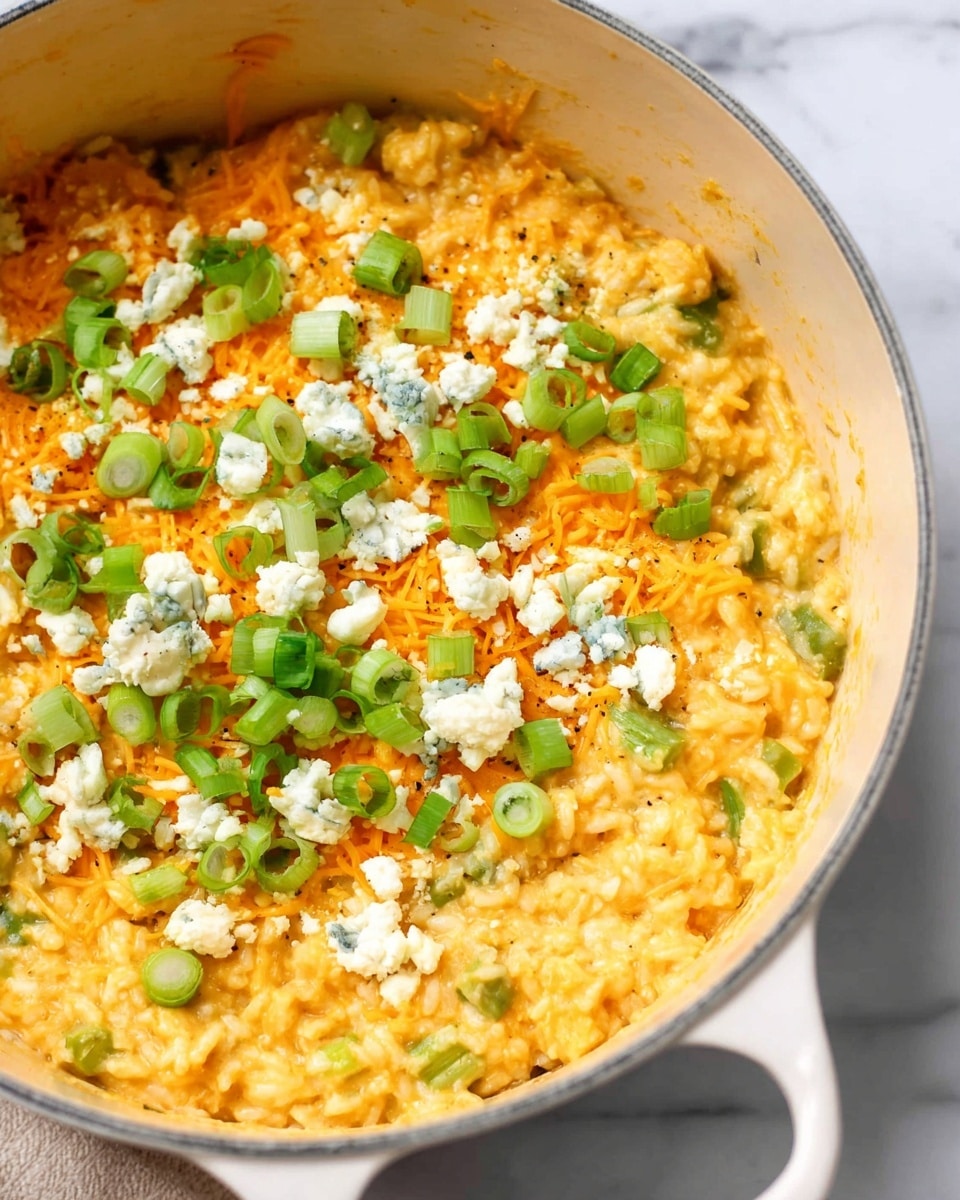 A close-up view of a creamy yellowish-orange rice dish in a white pot, showing mixed-in small green vegetable pieces. The top layer has shredded orange cheese, sprinkled white crumbled cheese with blue veins, and chopped bright green scallions scattered across. The rice texture looks soft and moist with visible grains, and the pot handles are visible on the sides. The surface beneath the pot has a white marbled texture. photo taken with an iphone --ar 4:5 --v 7
