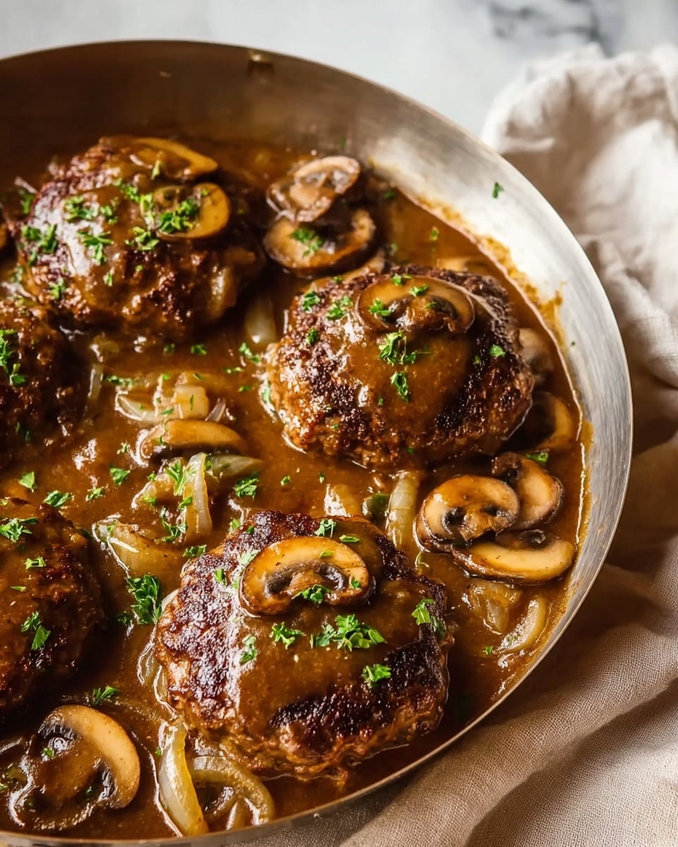 A close-up view of four thick, browned hamburger patties topped with sliced cooked mushrooms and chopped green herbs, sitting in a rich brown mushroom gravy that also has cooked onion slices and more mushrooms around the patties, all inside a metal pan. The pan is placed on a light-colored cloth, with a soft white marbled surface in the background. The sauce looks glossy and covers the patties evenly, making the whole dish look warm and hearty. Photo taken with an iphone --ar 4:5 --v 7