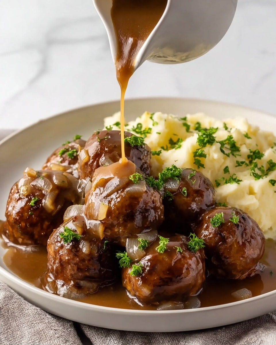 A white plate holds a serving of nine glossy brown meatballs with visible cooked onions scattered among them. The meatballs are covered in thick brown gravy that is being poured from a white jug, splashing onto the meatballs and pooling slightly on the plate. To the side of the meatballs, there is a portion of creamy mashed potatoes sprinkled with finely chopped green parsley. The meatballs are also garnished with small bits of green parsley on top. The background shows a white marbled texture. photo taken with an iphone --ar 4:5 --v 7